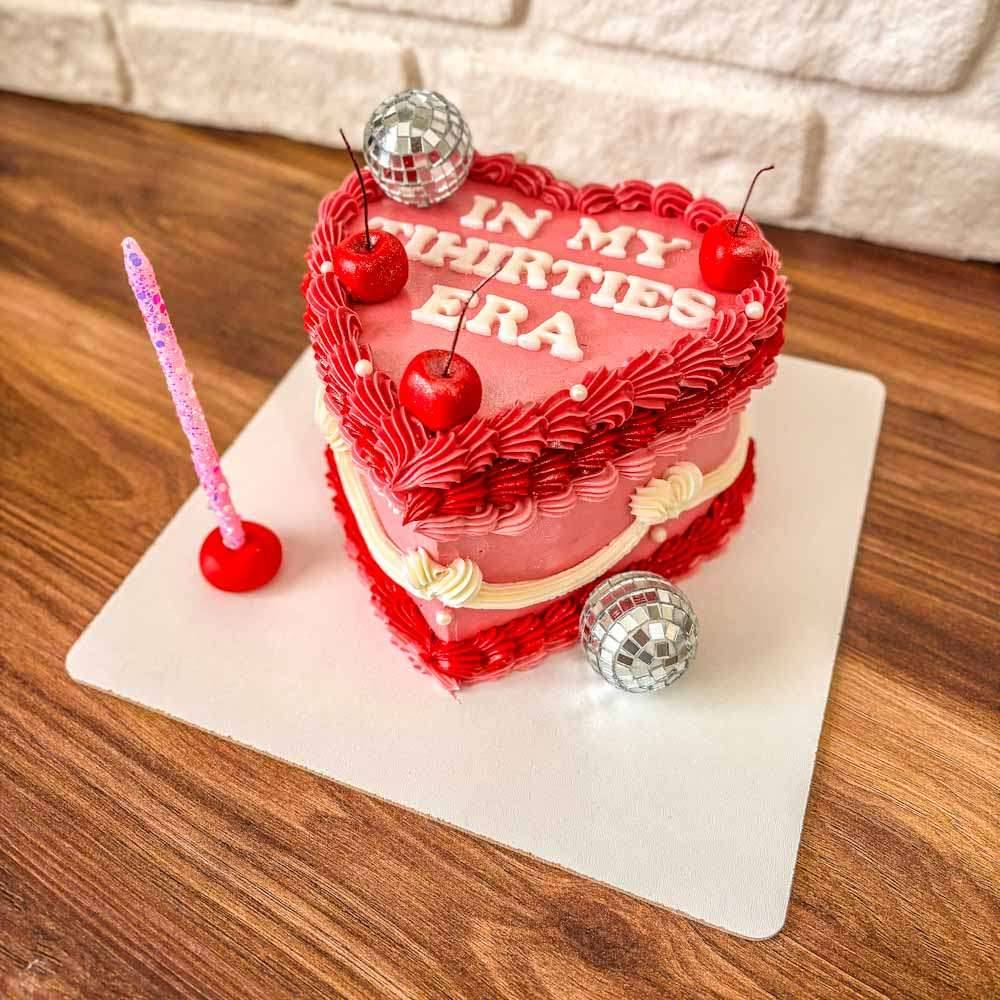 Beyaz zeminli vintage pasta, üstünde saplı kirazlar ve ışıltılı disko topu figürüyle süslenmiş; nostaljik ama enerjik bir tasarım.